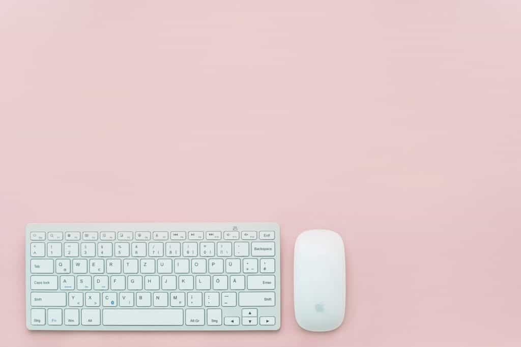 An Apple keyboard and mouse pictured on a pink background are work from home essentials