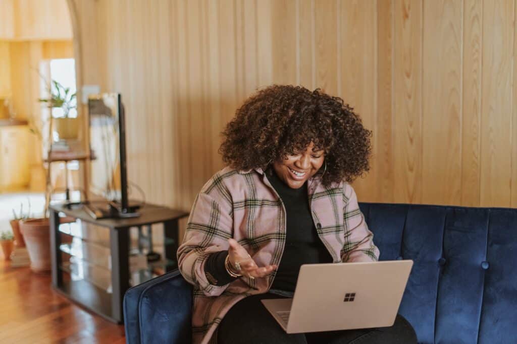 Young woman sitting on couch laughing at someone on laptop screen