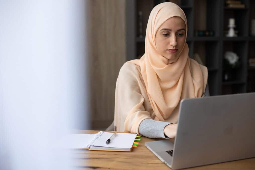 A freelance copywriter wearing a hijab working from home on laptop at their kitchen table