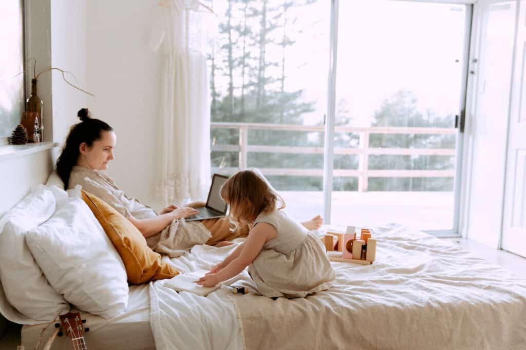 Mom working from home in bed on a laptop while child plays
